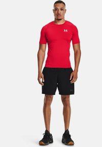Rotes, eng anliegendes Kurzarmhemd mit Logo, kombiniert mit schwarzen Shorts und schwarzen Turnschuhen. Glatte Textur, sportliches Design und knielange Shorts.