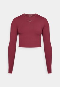 Burgundska dugmadna crop majica s dugim rukavima napravljena od glatkog, rastezljivog materijala. Ima okrugli izrez i mali bijeli logo na prsima.