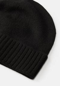 Gorro de malha preto com uma textura suave e punho canelado. O design apresenta um topo arredondado e é feito de um tecido macio e quente.