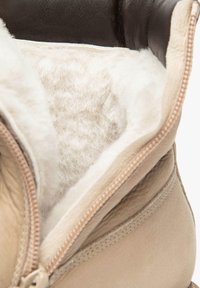 Botte beige avec une doublure en fourrure beige douce et des bords en cuir brun foncé, avec une fermeture éclair visible et une texture lisse.