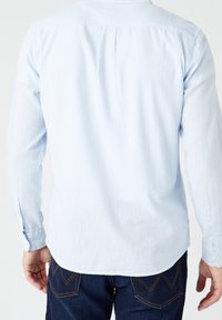 Camicia azzurro chiaro a maniche lunghe con righe bianche verticali, polsini con bottoni e orlo arrotondato, realizzata in un tessuto morbido e testurizzato.