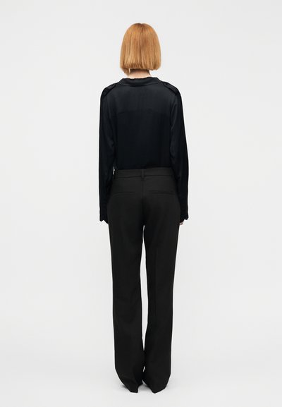 Μαύρο σατέν πουκάμισο με μακριά μανίκια και στρογγυλή λαιμόκοψη, με επιθέματα στους ώμους. Συνδυασμένο με ψηλόμεσα μαύρα παντελόνια με πλαϊνές τσέπες.