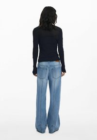 Navy gestreepte top met lange mouwen en een textuurpatroon, gecombineerd met lichtblauwe wijde jeans met achterzakken en een rafelige zoom.
