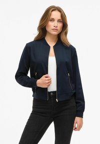 Veste de bombardier marine avec fermeture éclair à l'avant, poignets côtelés et deux poches zippées ; fabriquée en tissu lisse avec une coupe ajustée.