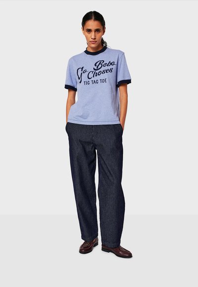 Camiseta de algodón azul clara con cuello y puños de canalé azul oscuro con texto en color negro. Combinada con pantalones de corte amplio a rayas en blanco y negro.