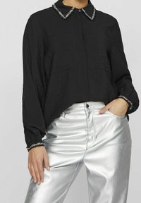 Black shirt with textured fabric, featuring a collar with metallic accents and elastic cuffs, paired with shiny silver pants.