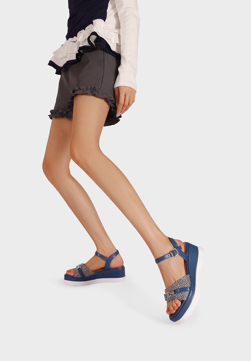 Sandali blu con un motivo intrecciato sulle cinghie, una suola platform bianca e una cinghia regolabile alla caviglia per una vestibilità sicura.