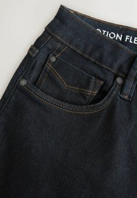 Mørk vask denim jeans med slim fit, der har fremtrædende orange syninger, en lille frontlomme og et mærke med teksten "Motion Flex."