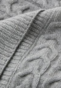 Szara dzianina o wzorze warkocza i fakturowanym splocie. Miękka, gruba przędza z różnorodnymi szczegółami ściegów nadającymi głębię.