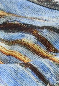 Close-up of textured fabric with wavy patterns in blue, brown, and beige tones, showing knitted stitch details and color variations.