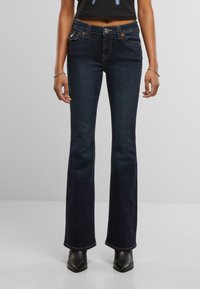 Jeans svasati di un blu scuro realizzati in denim, con un classico design a 5 tasche, cuciture arancioni sottili e chiusura con bottone in metallo.