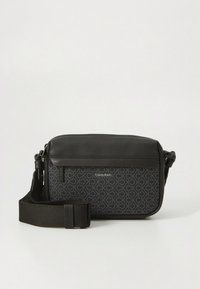 Black crossbody bag with adjustable strap, front panel featuring repeating "CK" pattern and "Calvin Klein" logo.