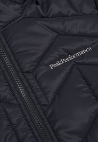 Navy quilted puffer vest with a diagonal pattern, featuring a black zipper and white "PeakPerformance" embroidery on the chest.
