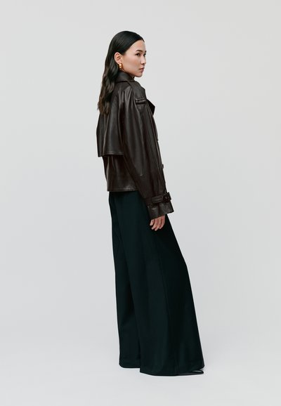 Braune Lederjacke mit breitem Revers und oversized Passform. Kombiniert mit lockeren schwarzen Hosen. Weiche Textur, minimalistische Details.