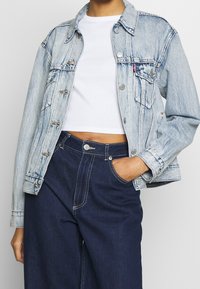 Ljusblå denimjacka med krage, framfickor och silverfärgad knäppning. Matchad med mörkblå högmidjade byxor med kontraststickningar.