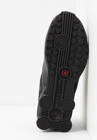 Black athletic shoe sole featuring a textured pattern, circular nodes, and grooves, with a visible red accent and brand text "NIKE SHOX."