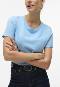 T-shirt azzurro chiaro a maniche corte in tessuto morbido con scollatura tonda. Abbinato a jeans scuri e una cintura nera con dettaglio in fibbia argentata.