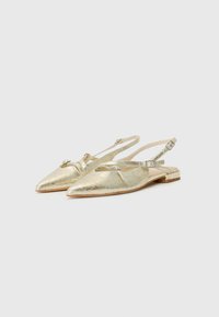 Spisse tå gullmetalliske slingback-sko med flatt hæl, med ankelreim og dekorative detaljer foran.