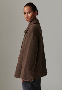 Brown textured jacket with frayed edges, large collar, and loose fit. Features a pocket on the front and a button closure.