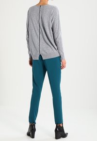 Grijze gebreide trui met een ritssluiting op de achterkant, gecombineerd met teal tapered broeken. Zwarte haklaarzen maken de outfit compleet.