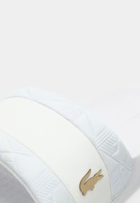 Άσπρο σανδάλι slide με υφή στο λουράκι και γεωμετρικό σχέδιο, με χρυσή λεπτομέρεια λογότυπου. Μινιμαλιστικό στυλ με μαλακό φινίρισμα.