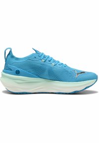 Zapatilla deportiva de color azul claro con una parte superior de punto texturizado, que presenta una entresuela blanca, un sistema de cordones y un acento de logo metálico en la punta.