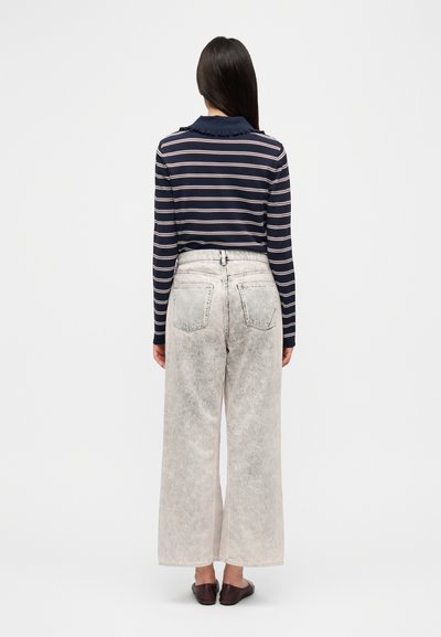 Ναυτικό μπλε και ριγωτό πουκάμισο με μακριά μανίκια και γιακά με βολάν, σετ με φαρδιά, ανοιχτόχρωμα ξεθωριασμένα τζιν και σκούρα παπούτσια τύπου slip-on.