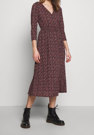 Blumige Wickelkleid in Dunkelrot mit Dreiviertelärmeln, V-Ausschnitt, elastischem Taillengummi und fließender Midi-Länge. Getragen mit schwarzen Schnürstiefeln.