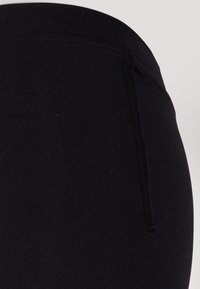 Juodos lengvos, prigludusios leggingai, pagamintos iš lygaus, tamprus audinys. Yra aukšta juosmens juosta ir šoninis siuvimo detalė. Nėra matomų logotipų ar raštų.