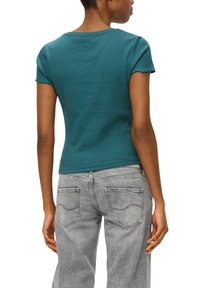 Türkisfarbene, taillierte T-Shirt mit kurzen Ärmeln, weichem Material und rundem Halsausschnitt, kombiniert mit hellgrauen Jeans, die über Gesäßtaschen verfügen.