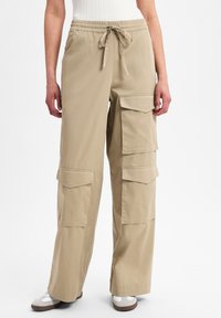 Beige cargo broek gemaakt van lichtgewicht stof, met meerdere grote zakken en een elastische tailleband met een trekkoordsluiting.