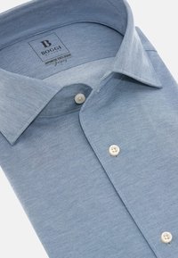 Camicia azzurro chiaro con texture uniforme, colletto aperto e bottoni color crema. L'etichetta all'interno del colletto riporta la scritta "Boggi Milano".