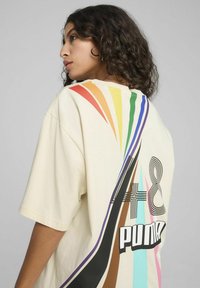 T-shirt oversize di colore crema con un motivo a strisce diagonali multicolori e il testo grafico "48 PUMA" sul retro. Tessuto in cotone morbido.