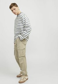 Gestreiftes Langarmhemd in Blau und Weiß, hellbeige Cargo-Hosen mit Seitentaschen und beige Sneaker mit braunen Akzenten.