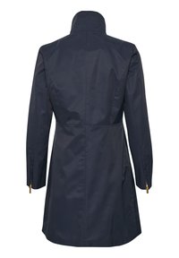 Mørkeblå vandtæt frakke med høj krave, tætsiddende talje og lange ærmer. Har guld lynlåse ved ærmerne og en glat tekstur.