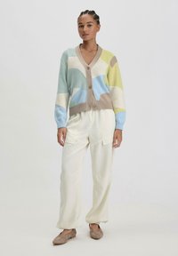 Gehaakte cardigan in pasteltinten, met geometrische patronen, een V-hals en knoopsluiting; gecombineerd met crèmekleurige wijde broek.