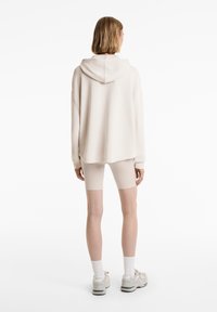 Hoodie oversize beige clair avec une capuche, des poignets côtelés et une coupe décontractée. Associé à un short de vélo beige clair. Design minimaliste.