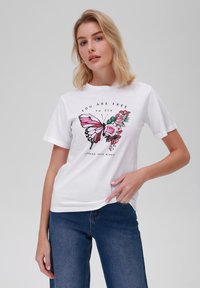 Bílý bavlněný tričko s velkým potiskem růžové motýla a růží, s textem "JSI VOLNÝ, abys létal" v černém písmu.