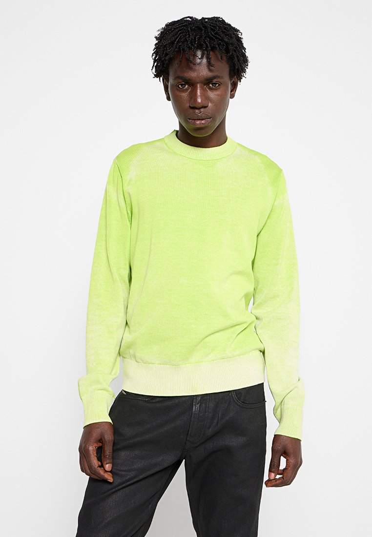 Limegrüner Pullover aus weichem, strukturiertem Stoff, mit einem gerippten Rundhalsausschnitt und Bündchen, kombiniert mit dunklen Hosen.