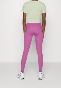 Hellgrünes Crop-Top mit kurzen Ärmeln, kombiniert mit enganliegenden pinken Leggings und weißen Turnschuhen mit pinken Akzenten.
