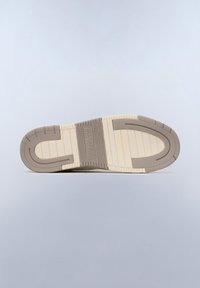 Sula av skon med en beige bas och bruna accenter. Har spår för grepp och varumärket embossed i mitten.