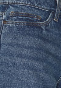 Denim jeans in medium blue with a textured finish, featuring orange stitching and a small front pocket.