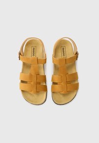 Sandales en cuir marron avec plusieurs brides horizontales, une bride arrière pour la cheville et une semelle intérieure en suède texturé. Design simple avec une semelle plate.