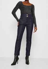 Mörkblå högmidjade jeans med kontrasterande gyllene sömmar, med framfickor och dubbelknäppning. Matchat med en glittrig svart topp.