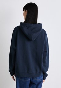 Felpa con cappuccio di colore blu navy con una vestibilità comoda. Presenta una tasca a marsupio, polsini a coste e dettagli di cucitura. Materiale in cotone morbido e strutturato.