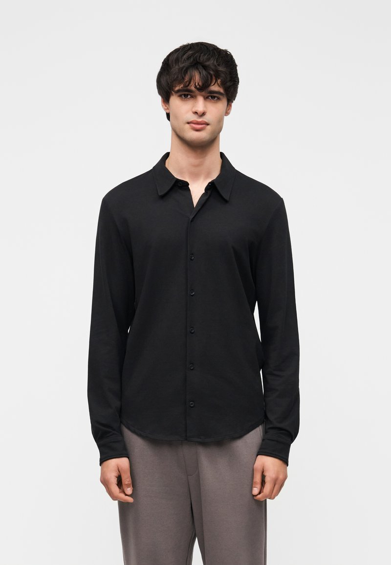 Μαύρο πουκάμισο μακρυμάνικο με γιακά με κουμπιά, κατασκευασμένο από λείο ύφασμα. Διαθέτει ευθεία άκρη και διακριτικό μπροστινό κούμπωμα με κουμπιά.