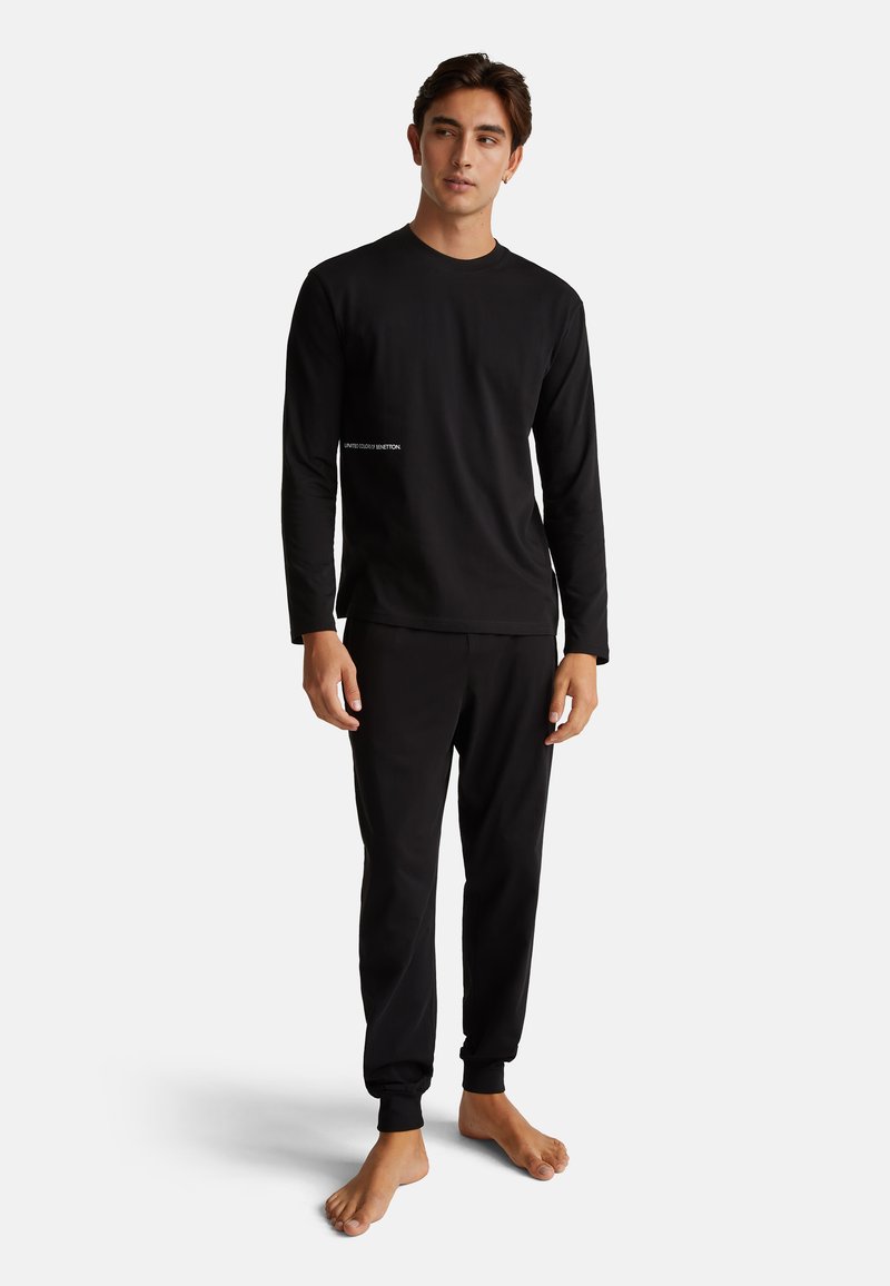 Zwarte lange mouwen shirt en bijpassende broek, gemaakt van een gladde stof. Bevat een klein logo op het shirt. Aansluitende manchetten op de broek.