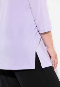 Top viola a tre quarti con un fit rilassato, fessure laterali e tessuto leggero e morbido. Indossato con pantaloni neri.