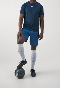 Nike idrottskläder: marinblå t-shirt med kort ärm, blå shorts, vita fotbollstrumpor och svarta fotbollsskor. Stående på en svart fotboll.