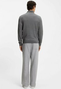 Pull gris en maille avec un col haut, associé à un pantalon gris ample, présentant une texture lisse et un design minimaliste.